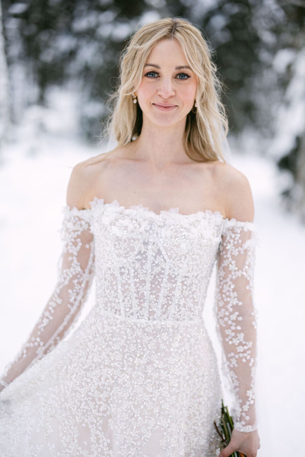 Woman in ornate off-shoulder wedding dress standing in a snowy landscape