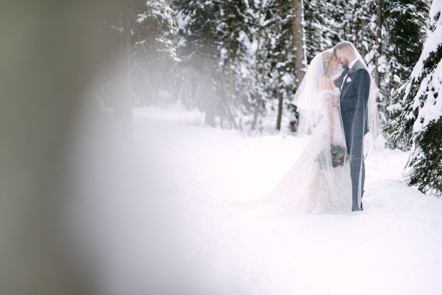 A couple in wedding attire sharing a tender moment in a snowy forest setting