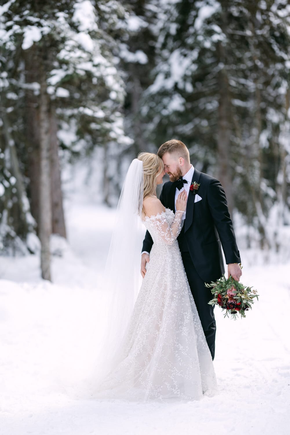 A bride and groom sharing an intimate moment amidst a snowy forest setting.