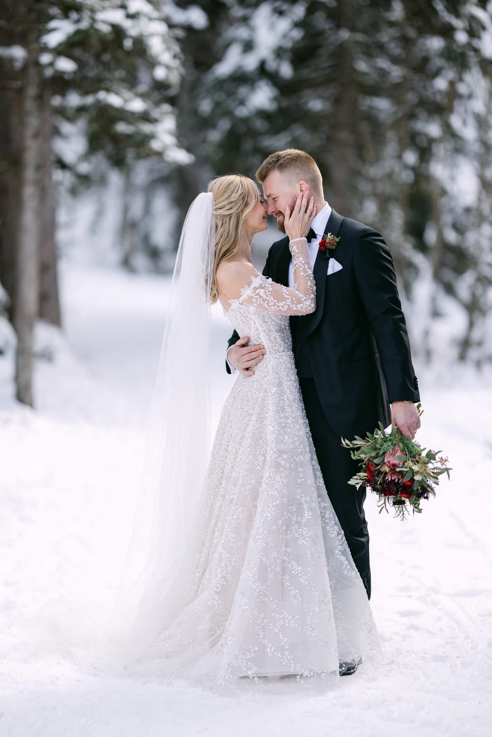 A bride and groom sharing a kiss in a snowy forest setting.