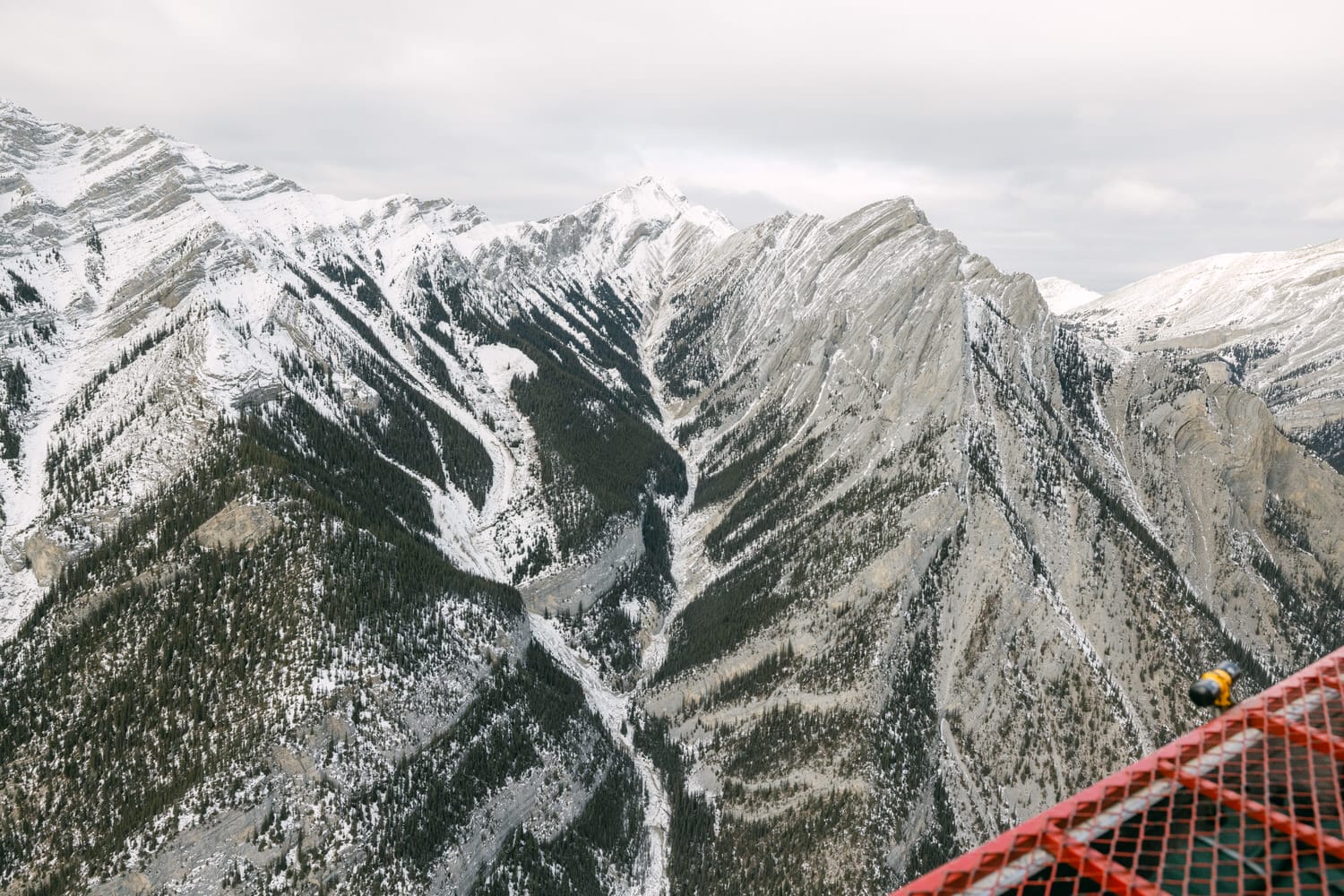 A breathtaking view of a snow-dusted mountain range with a partially visible person looking out from an observation deck.