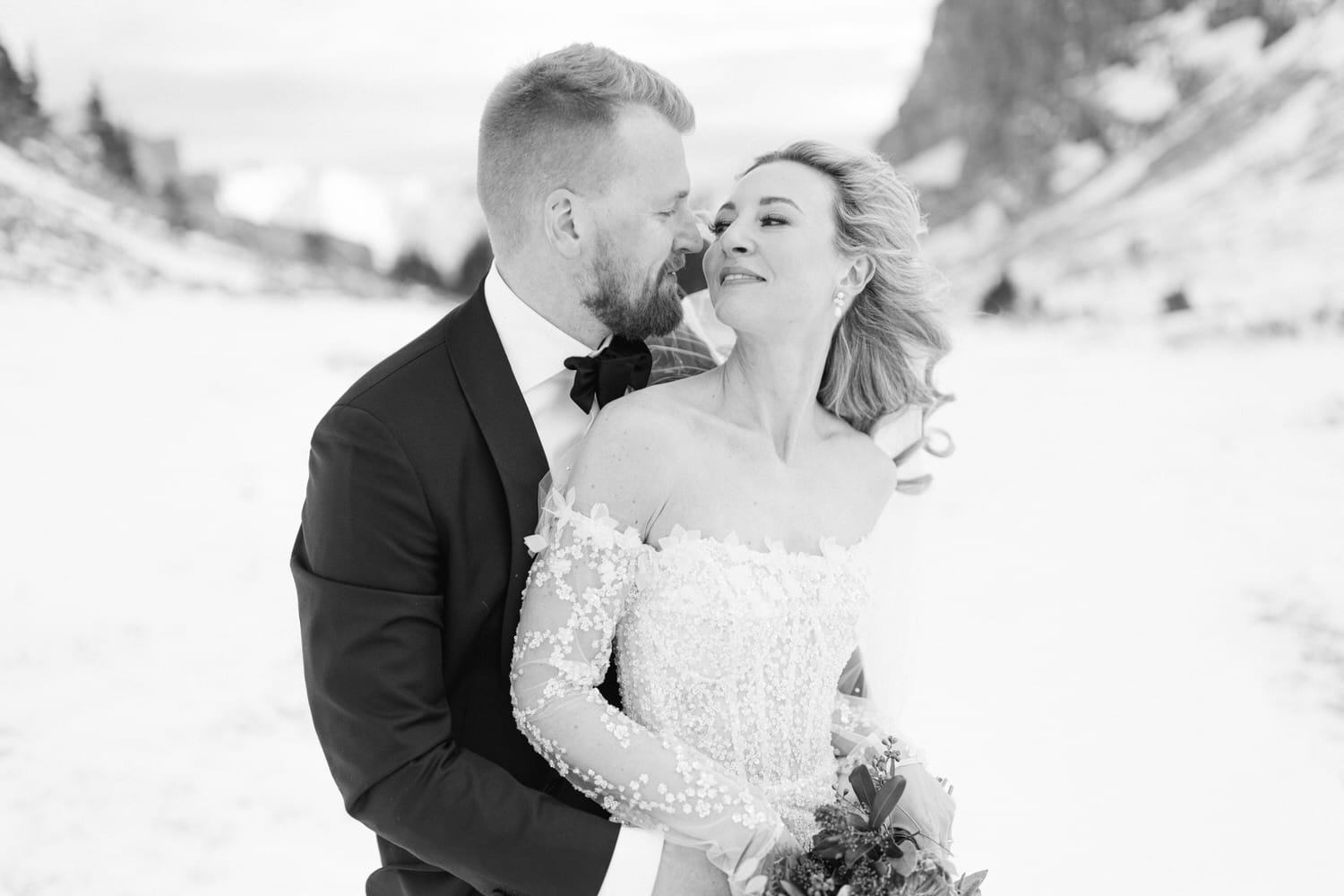 A black and white photo of a bride and groom embracing in a snowy landscape.