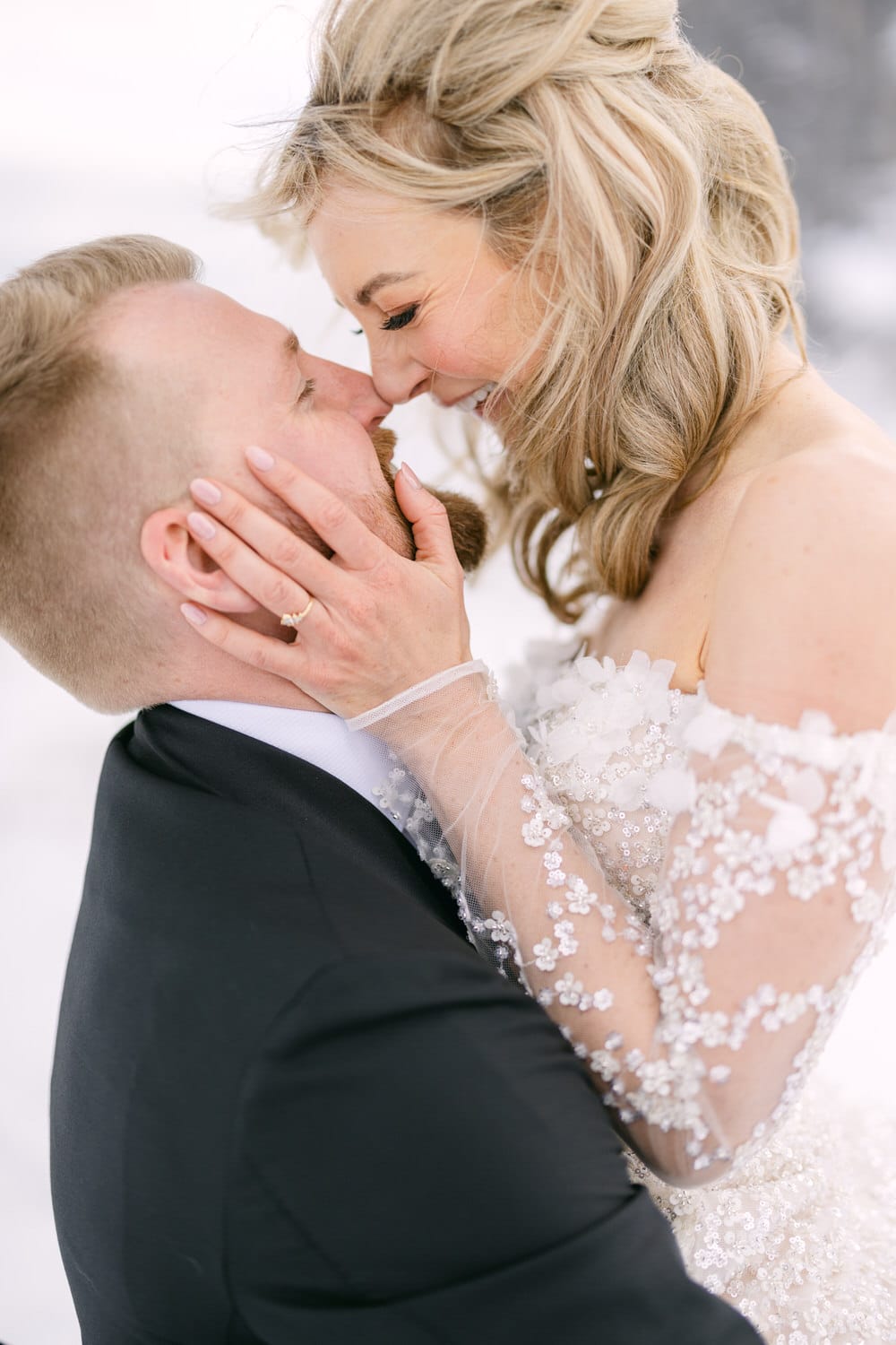 A bride and groom sharing a tender moment in a snow-kissed setting, with the bride gently holding the groom's face as they are about to kiss.