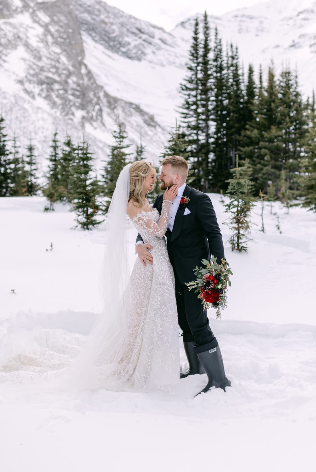 Bride and groom embracing in snowy mountain landscape.