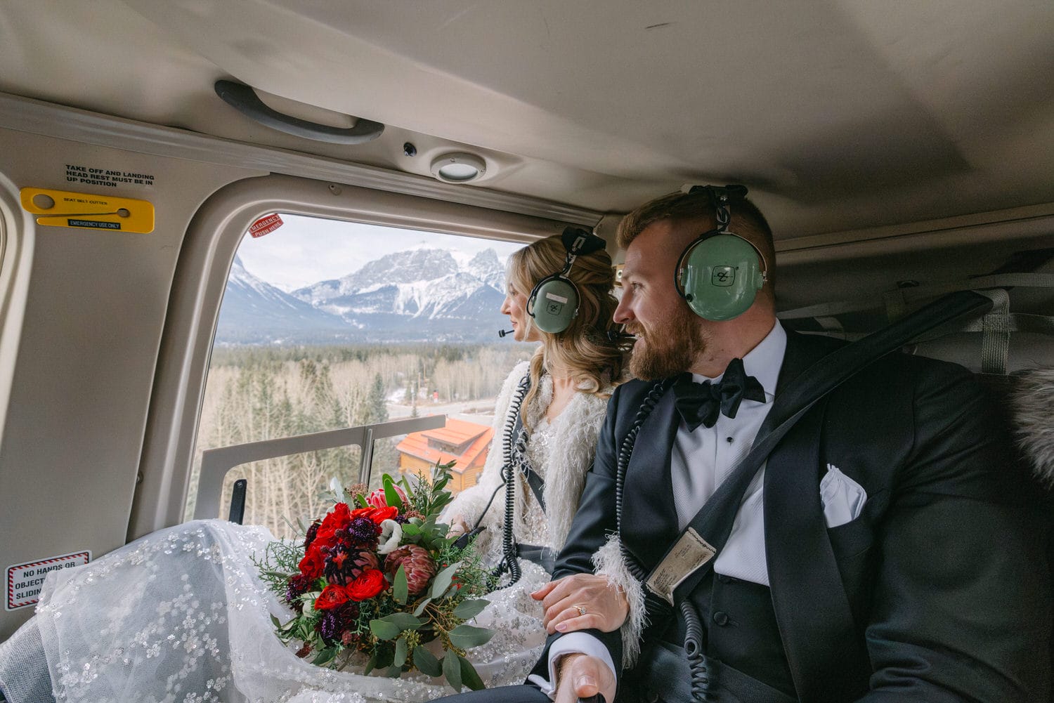 Bride and groom wearing headsets admiring the view from a helicopter cabin with scenic mountain backdrop