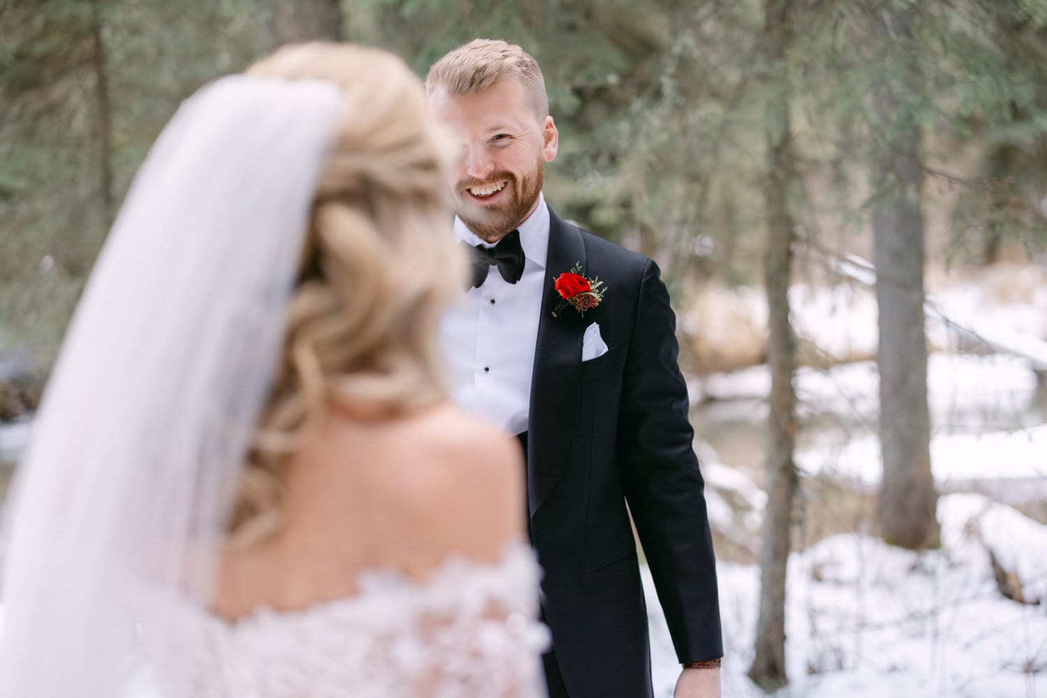 Groom smiling at the bride in a snowy forest setting