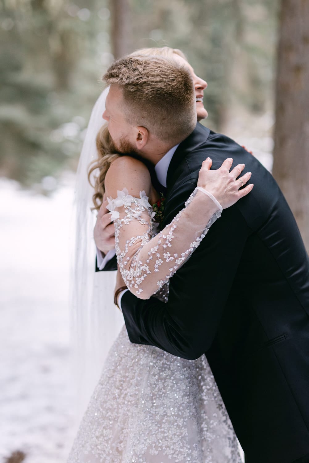 Bride and groom sharing an intimate embrace in a pine forest setting.