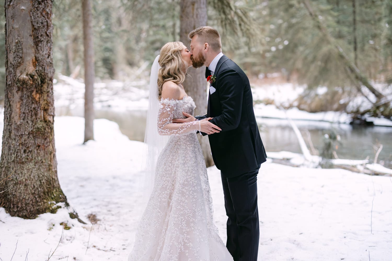 A bride and groom sharing a kiss in a snowy forest setting