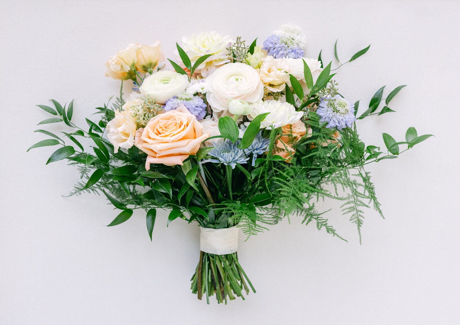 A lush bouquet with a variety of flowers including roses and hydrangeas, accented with greenery against a white background.