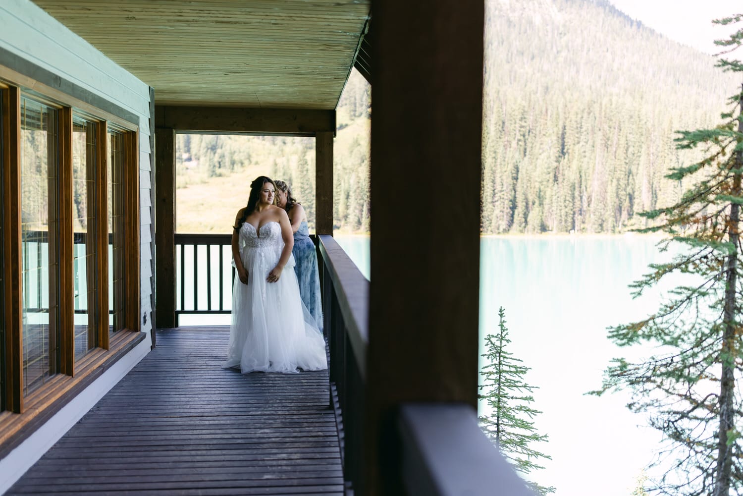 Two individuals in formal attire sharing a moment on a balcony overlooking a serene lake with forested hills in the background