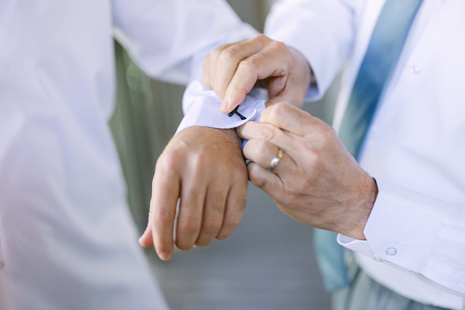 A close-up shot of a person fastening a black cufflink on a white shirt sleeve, typically part of formal attire preparation.