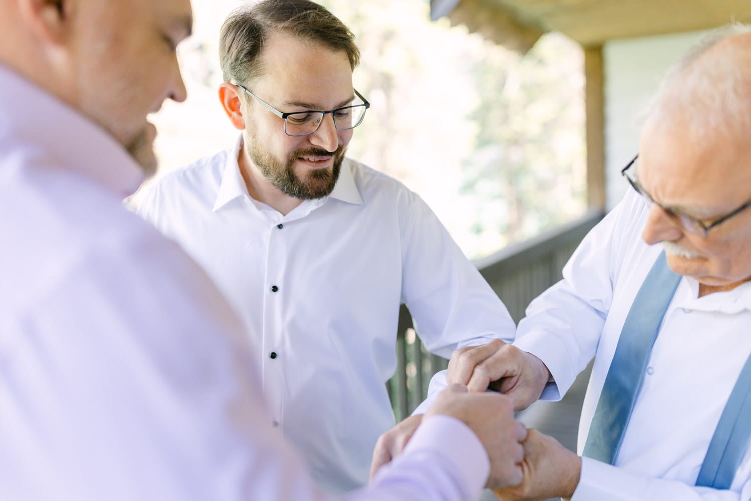 Close up of three men in white shirts, one looking at his watch while the others observe, outdoors on a bright day.