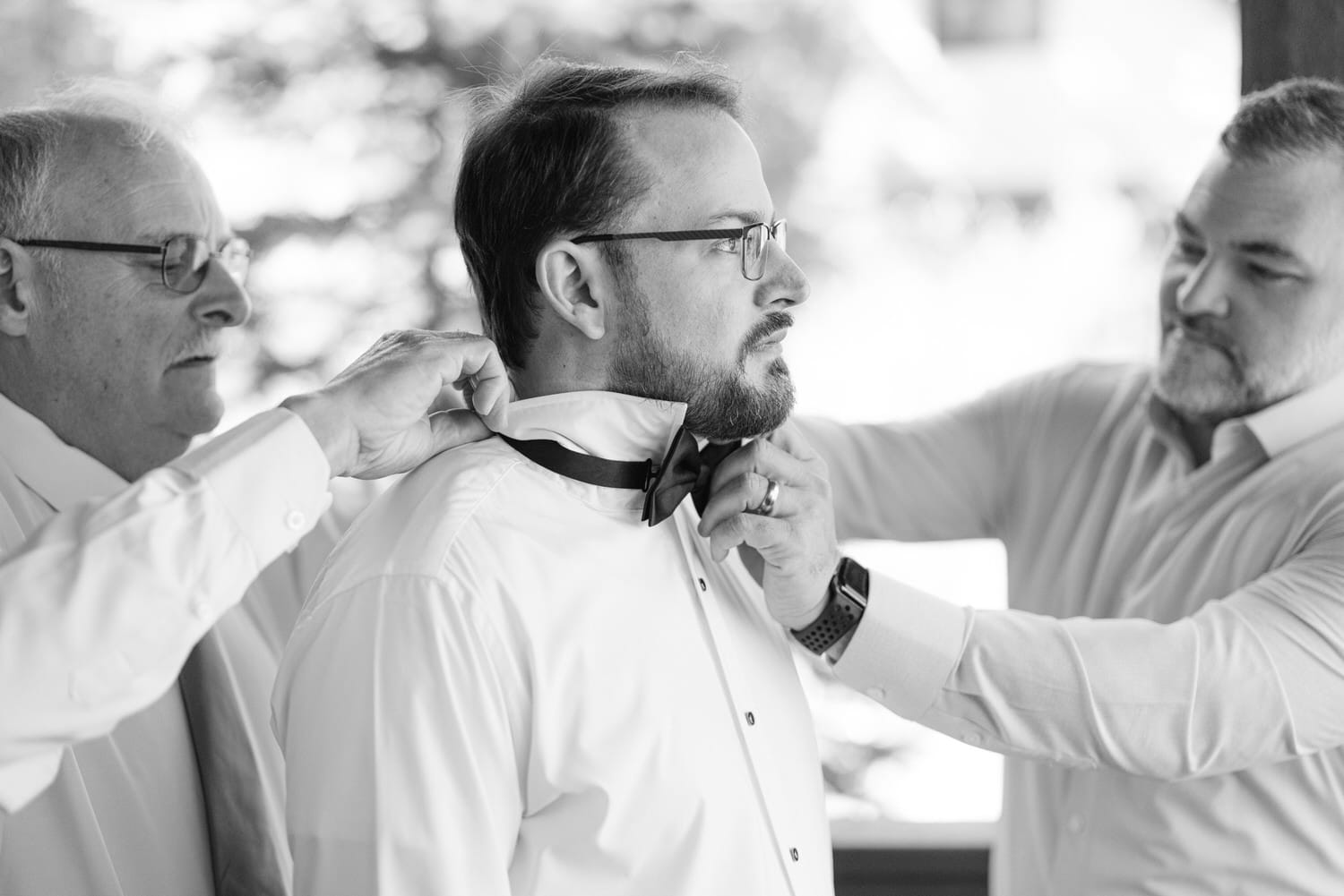 Two men assisting another man with his bow tie, all are dressed in formal white shirts, black and white photo.