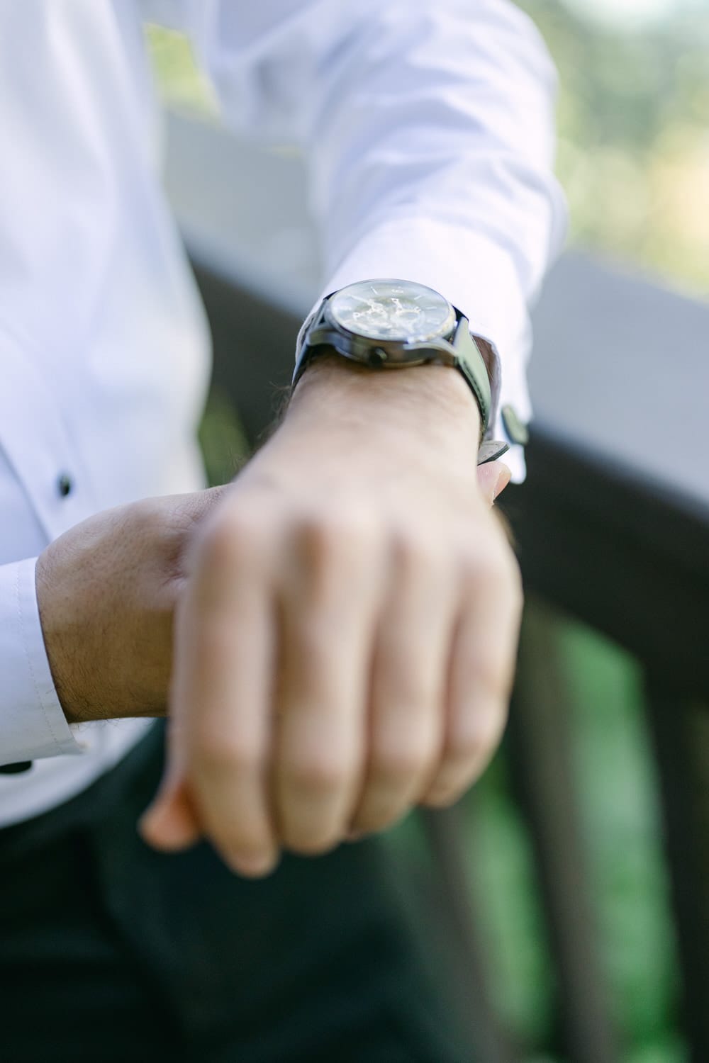 Close-up of a person's arm wearing a stylish watch with a focus on the watch face, against a blurred natural background.