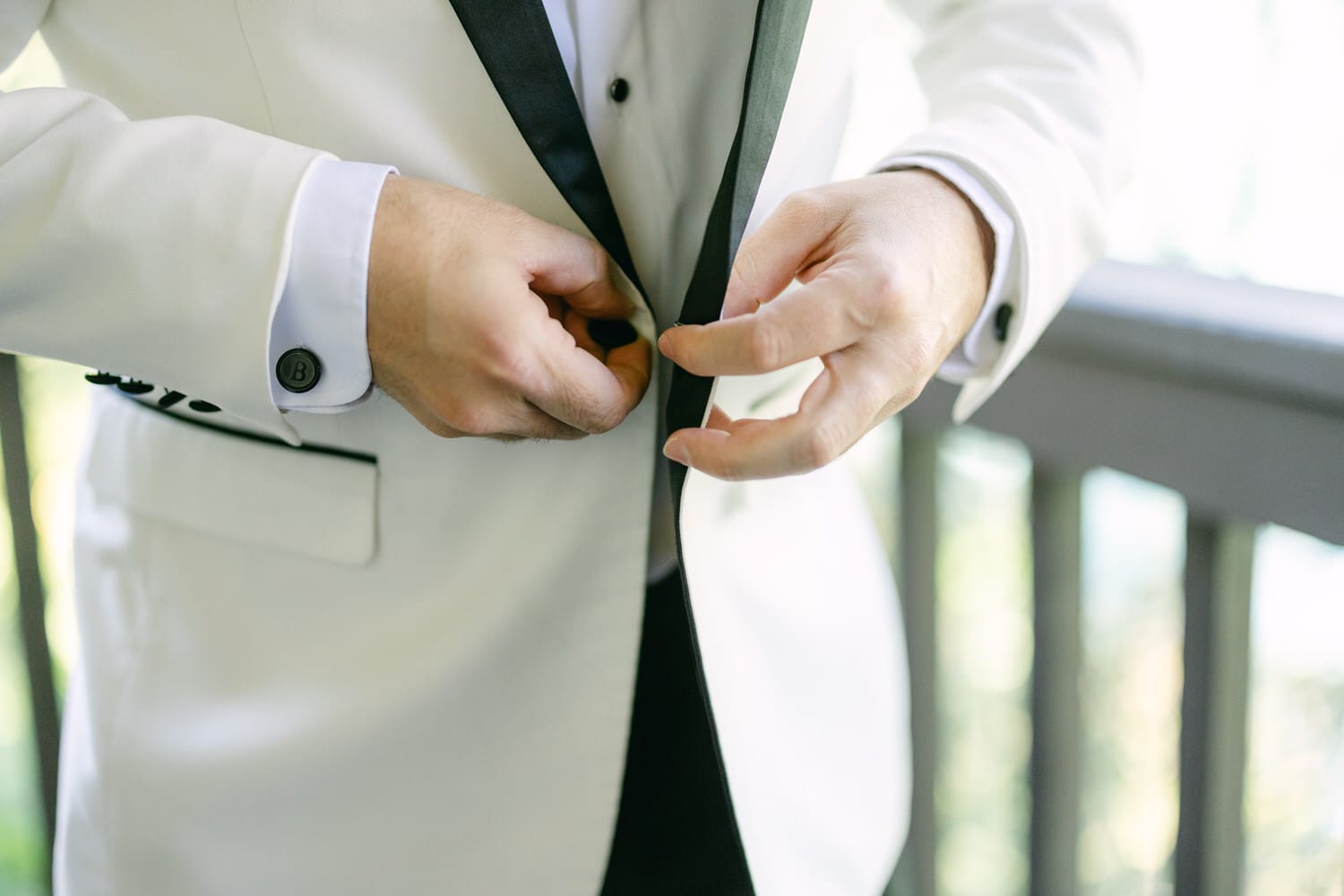 Close-up of a groom adjusting his cufflink while wearing a white tuxedo jacket