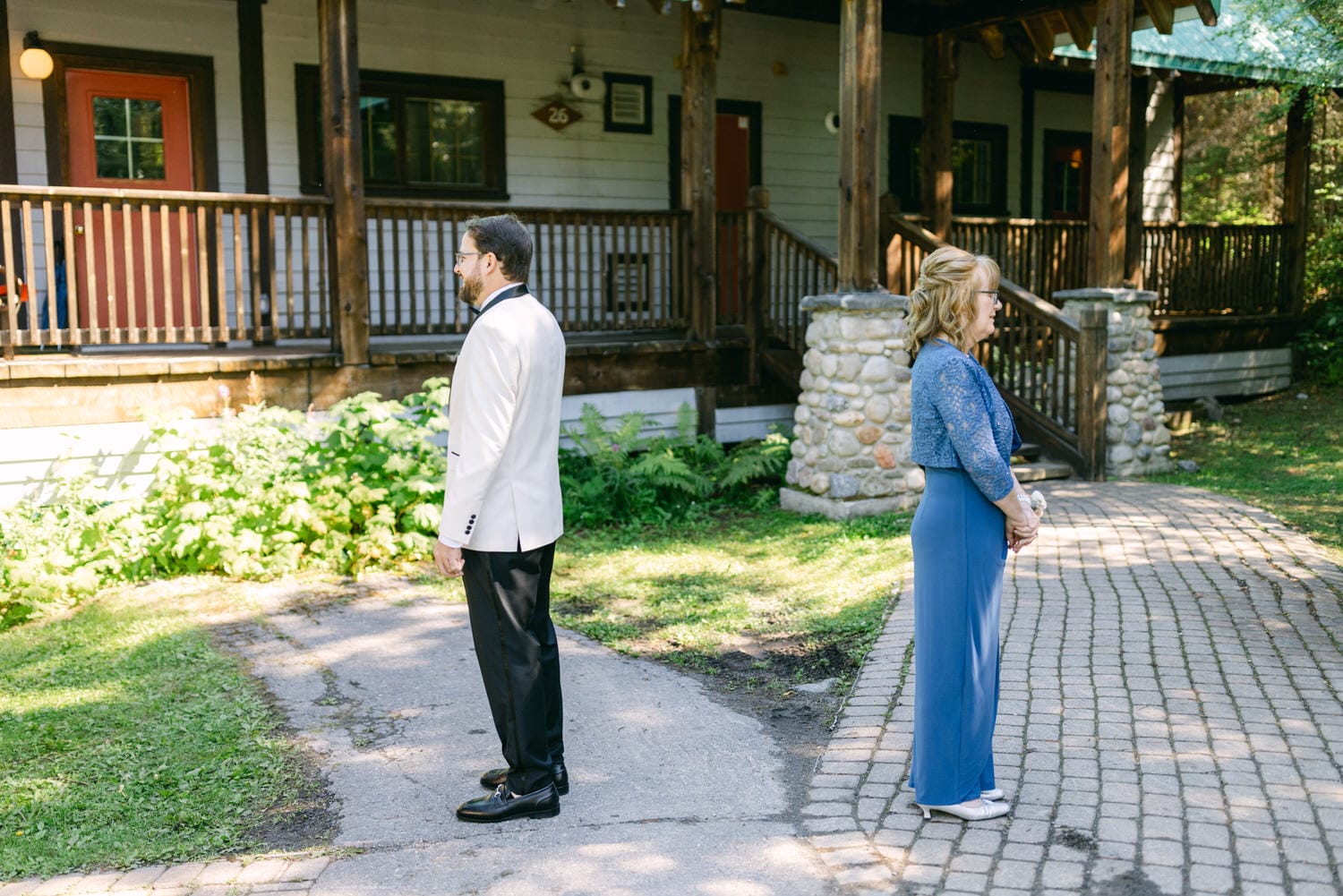 Two people standing apart facing different directions outside a rustic building with a wooden porch