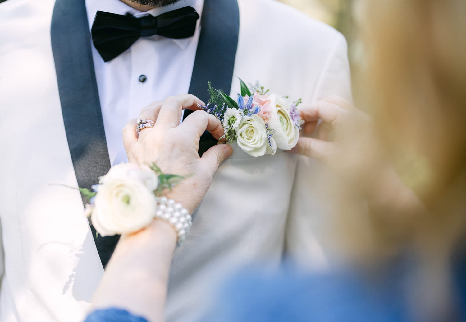 Close-up of hands pinning a floral boutonniere on the groom's lapel during a wedding ceremony