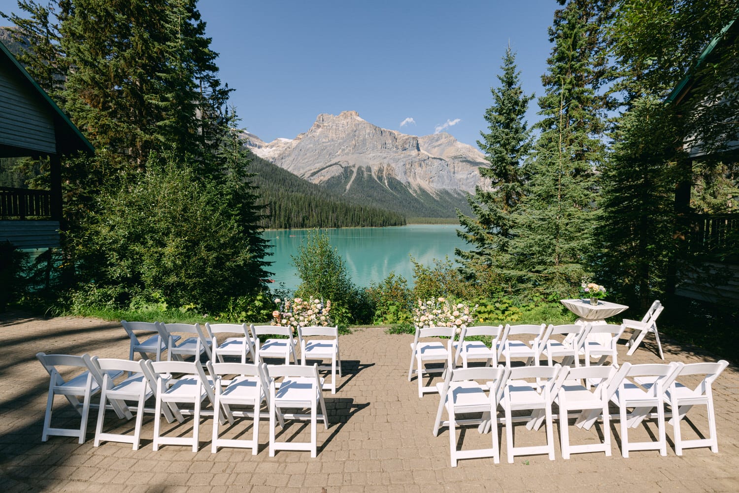 Rows of white chairs set up for a wedding ceremony with a stunning turquoise lake and mountain backdrop