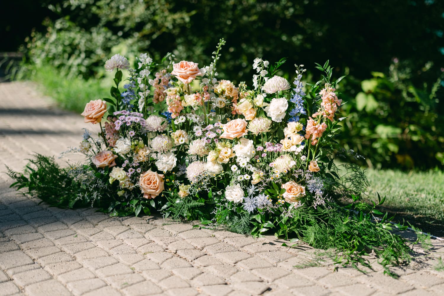 An arrangement of various colorful flowers, including roses, along a brick garden path surrounded by greenery.