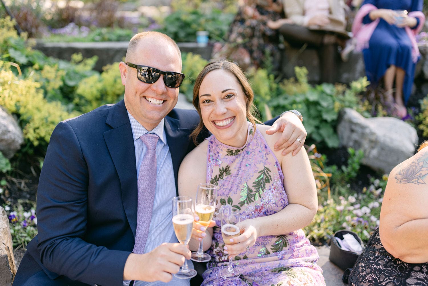 A man and woman smiling and toasting with champagne flutes at an outdoor social gathering.