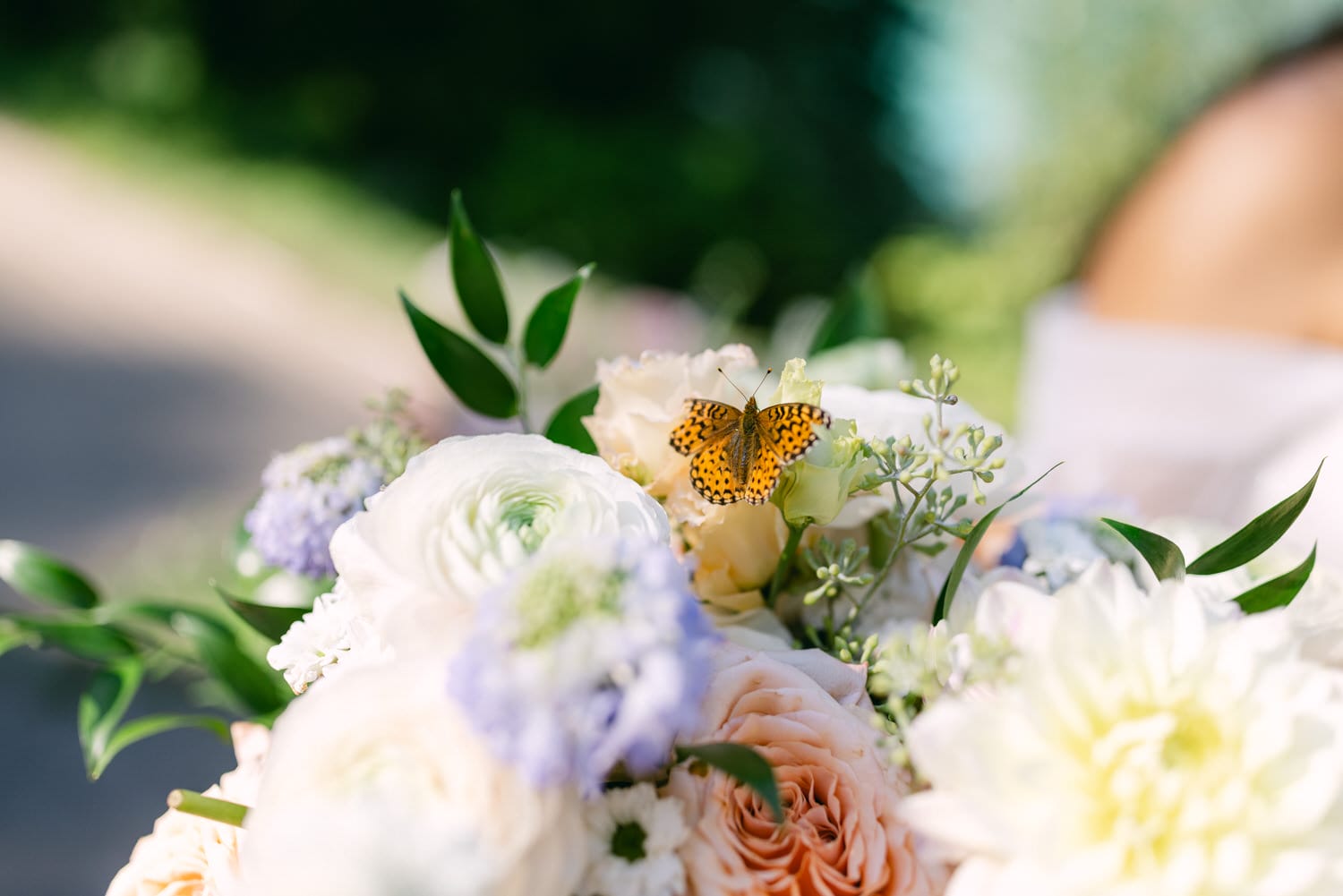 A close-up of a colorful butterfly perched on a beautiful bridal bouquet of white and pastel flowers.