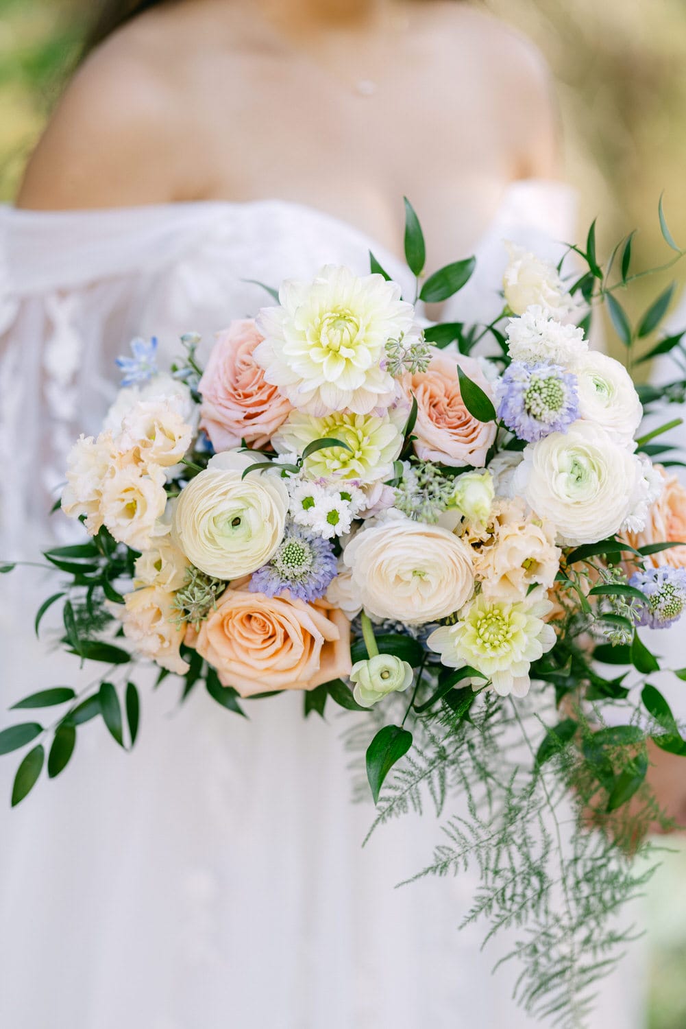 A bride holding a beautiful bouquet with a mix of white, peach, and purple flowers, with green foliage accents.