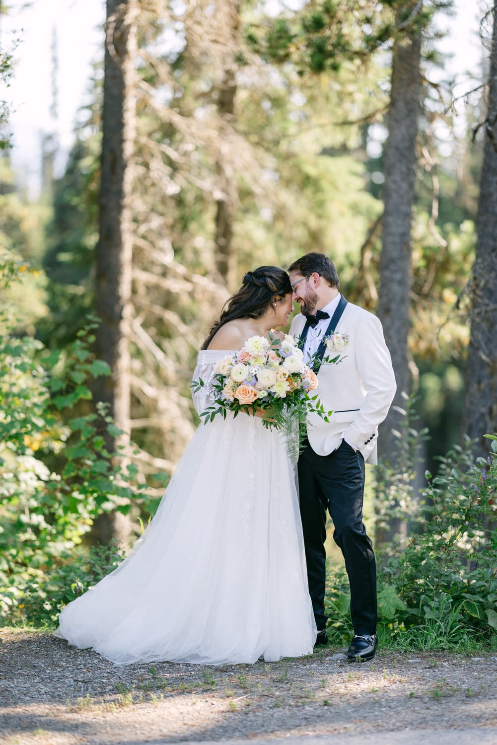 A bride and groom sharing a tender moment in a forested setting with the bride holding a bouquet of flowers.