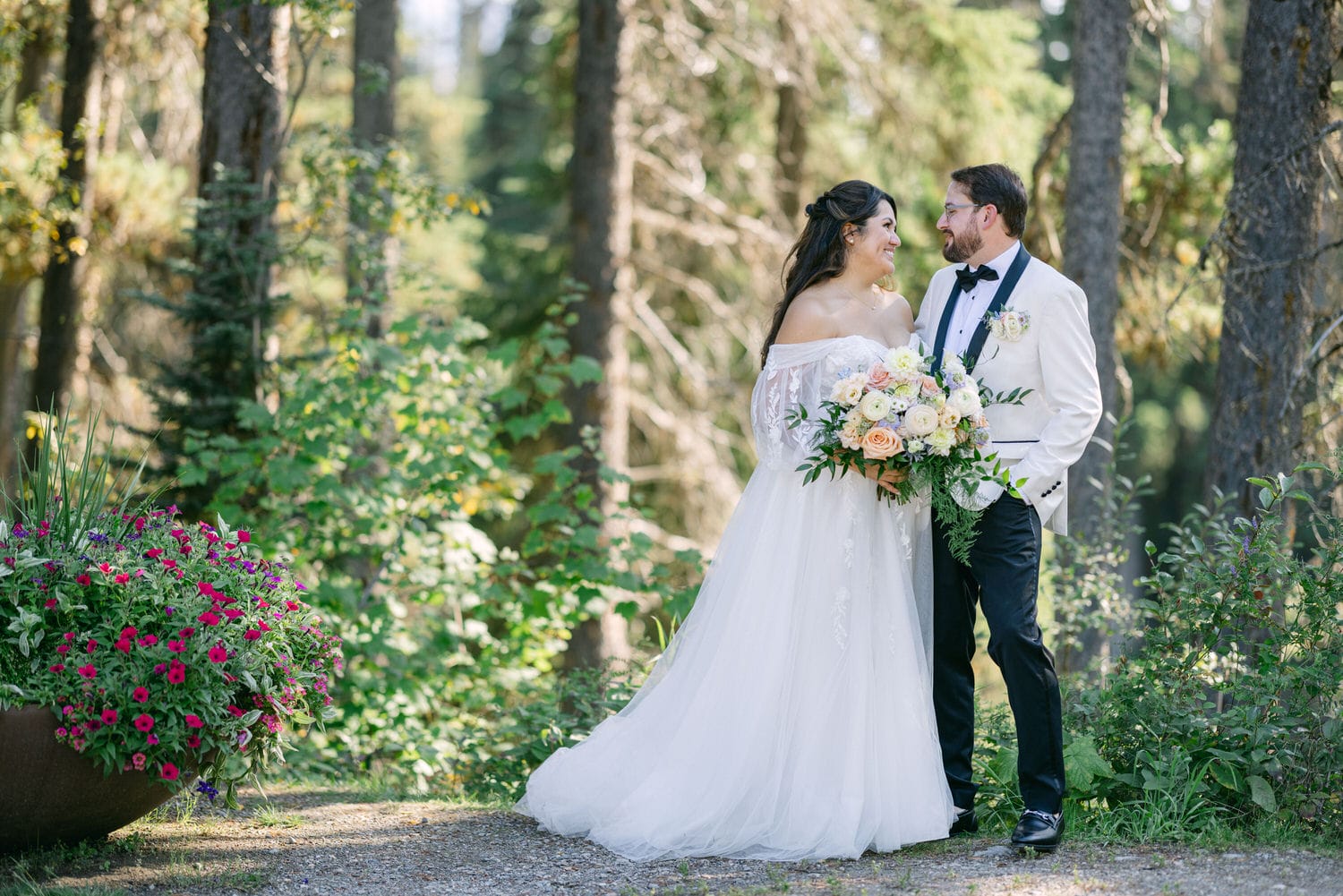 A bride and groom sharing a tender moment in a sunlit forest, with the bride holding a bouquet of flowers.