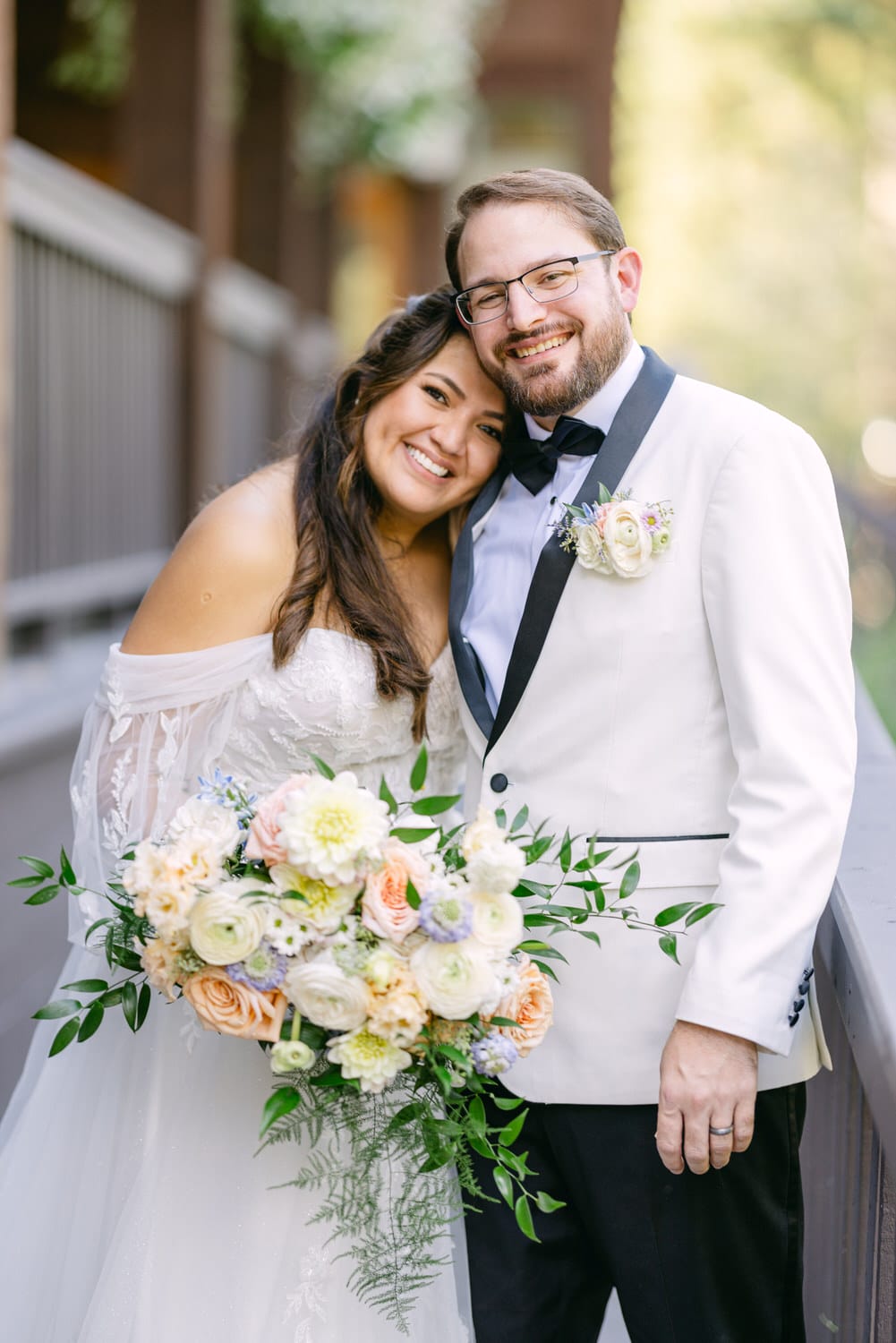 A happy bride and groom smiling and embracing on their wedding day, with the bride holding a bouquet of flowers.