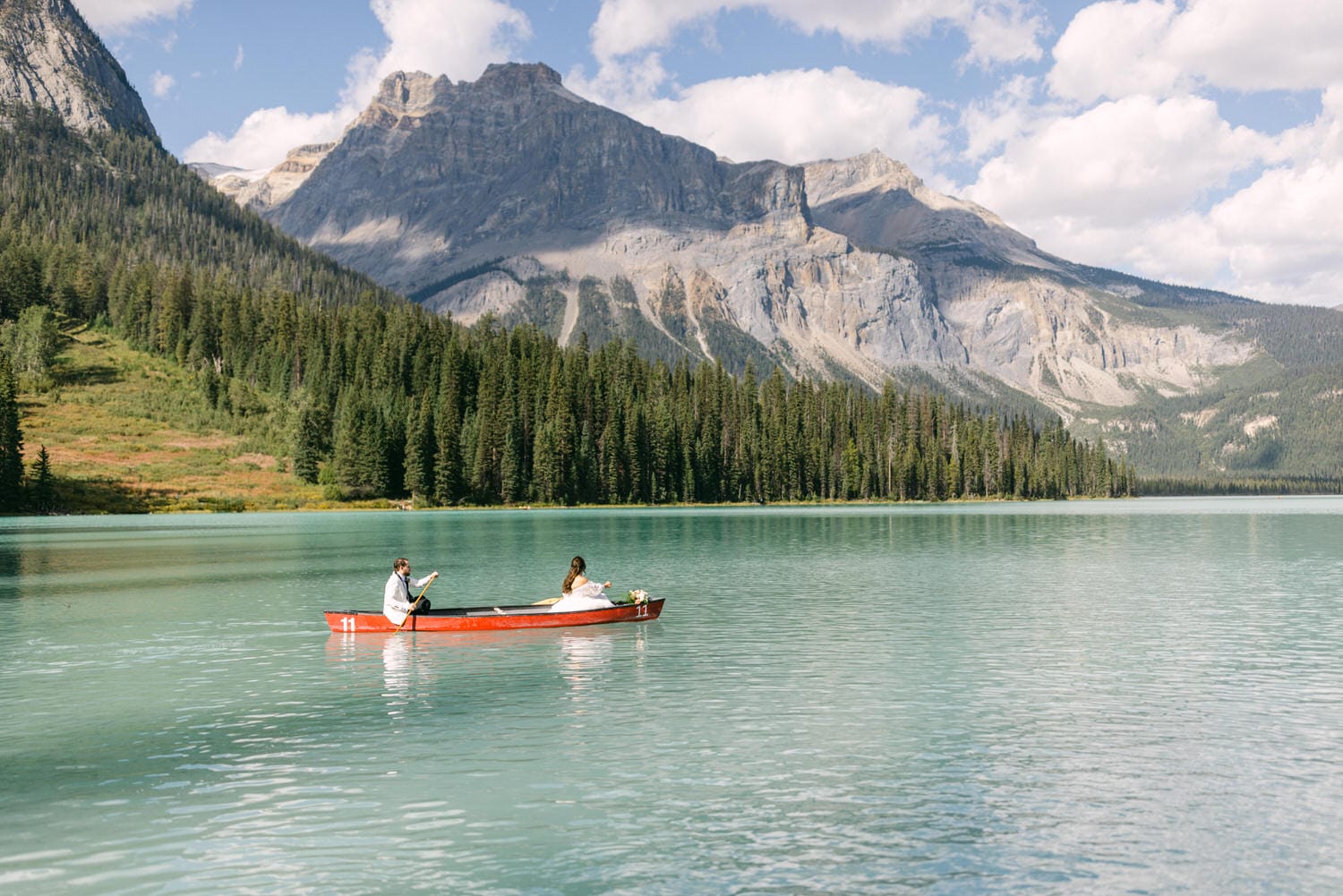 Two people paddling a red canoe on a calm turquoise lake with forested mountains in the background