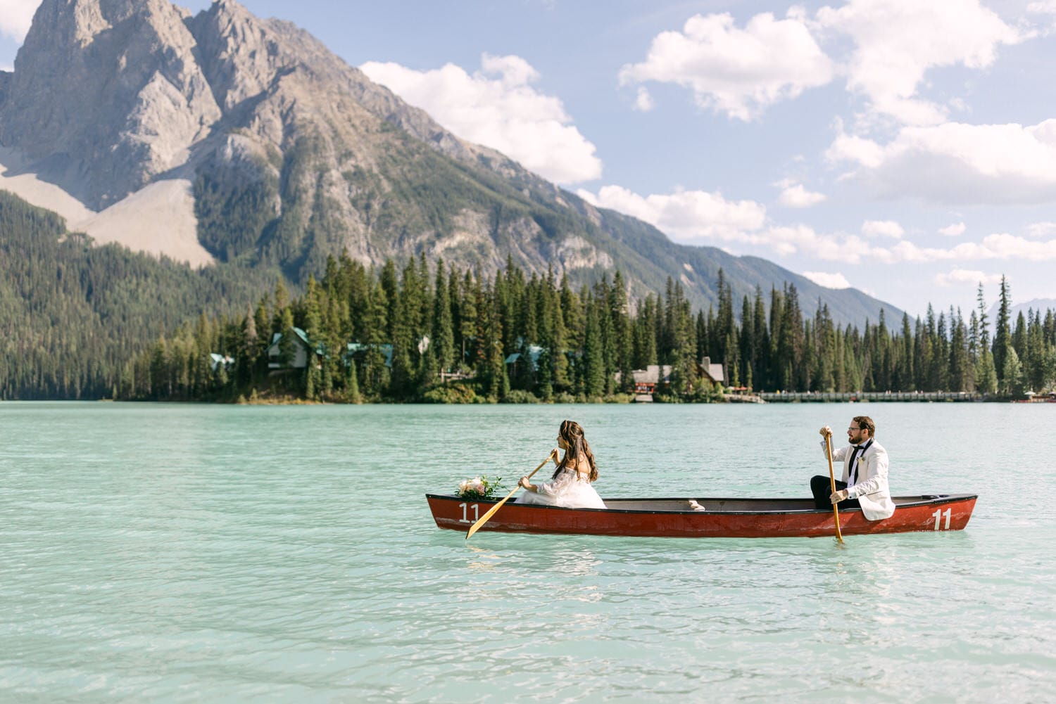 A bride and groom enjoying a serene moment rowing a canoe on a picturesque mountain lake.