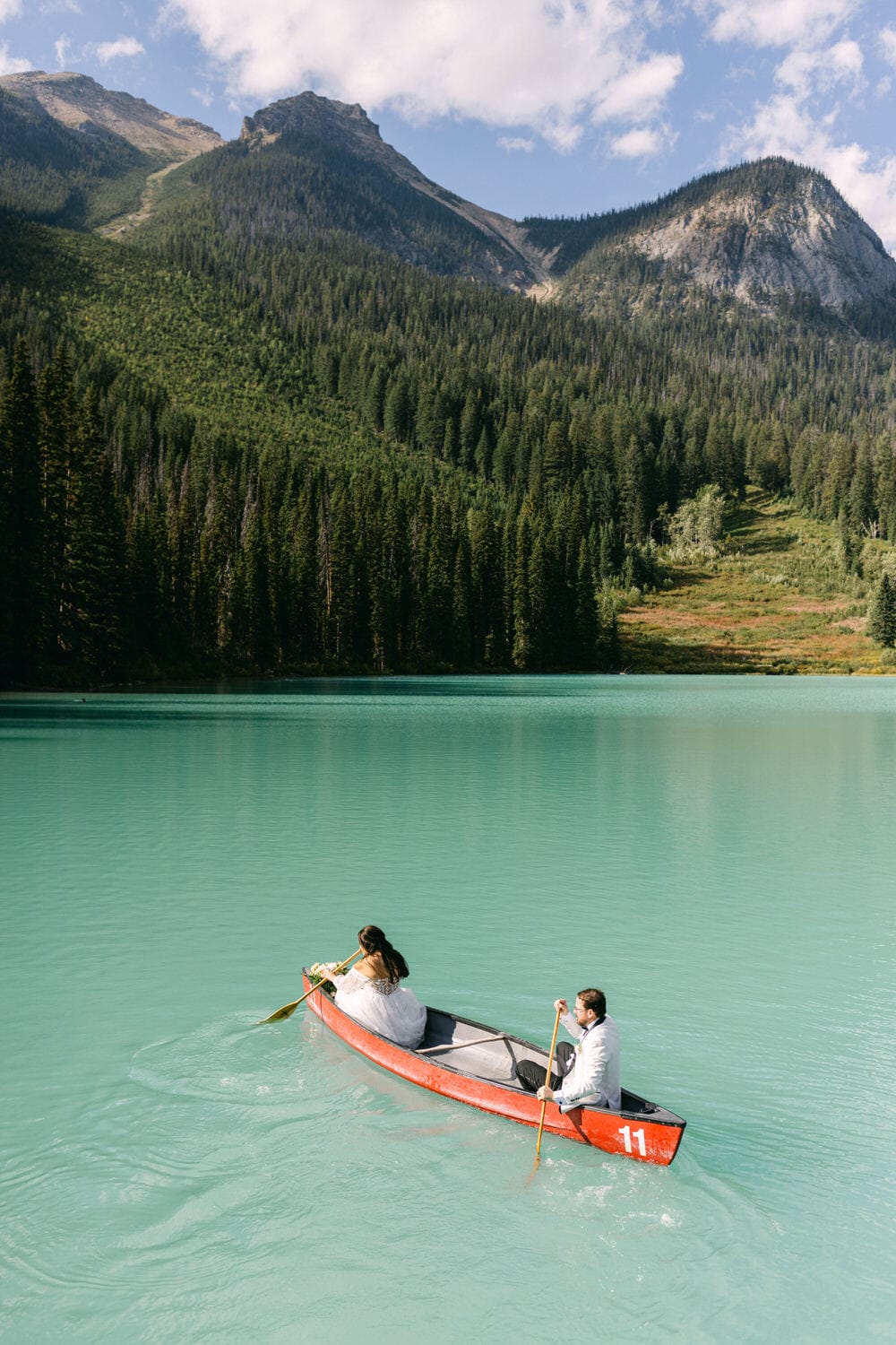 Two people paddling a red canoe on a calm turquoise lake with lush green mountains in the background.