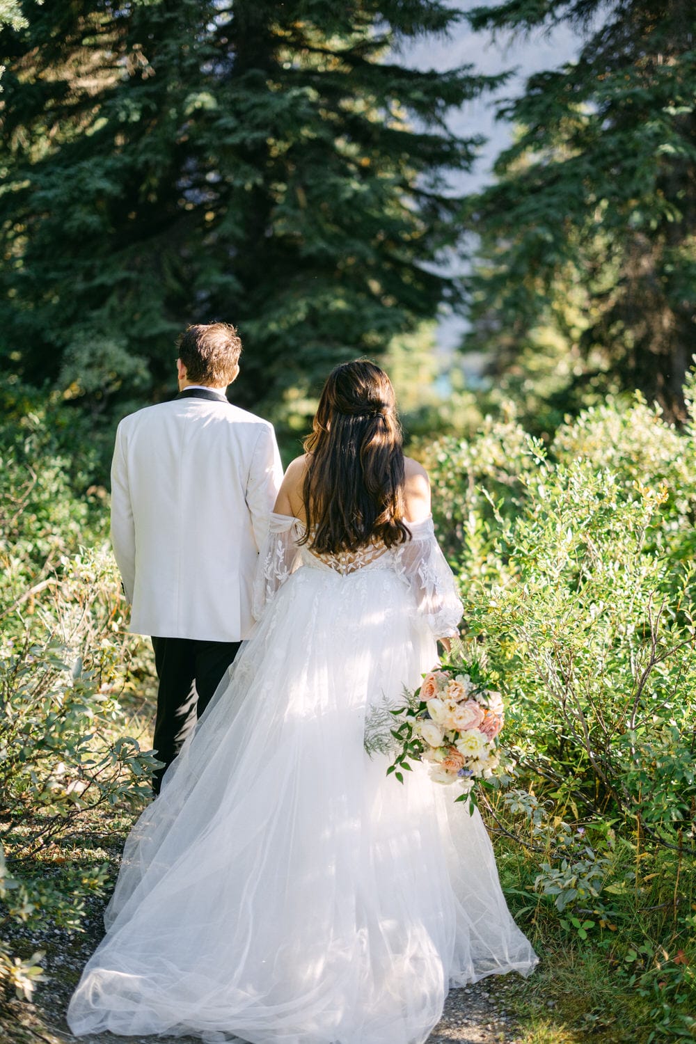 A bride and groom walking hand in hand down a garden path surrounded by greenery.