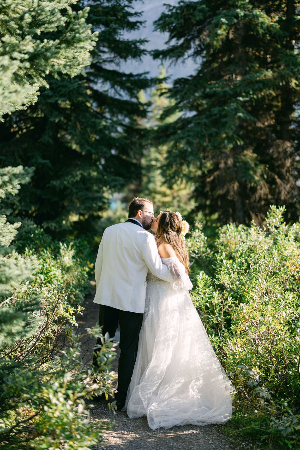 A bride and groom holding each other while walking through a picturesque forest pathway.