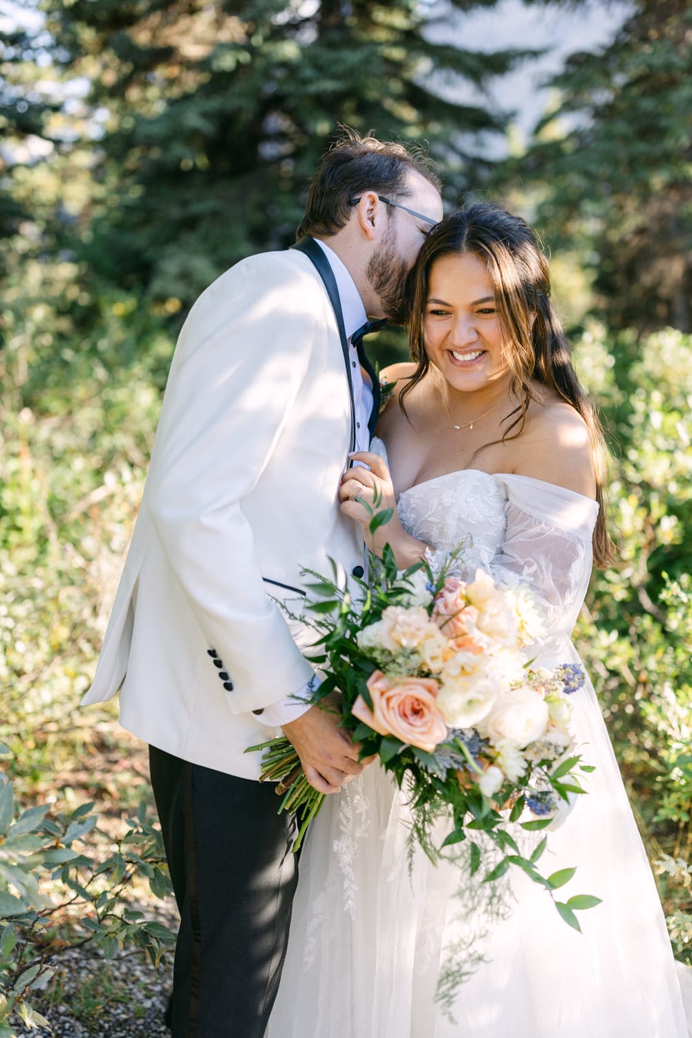 A bride and groom sharing a loving embrace outdoors, with the bride holding a bouquet of flowers.