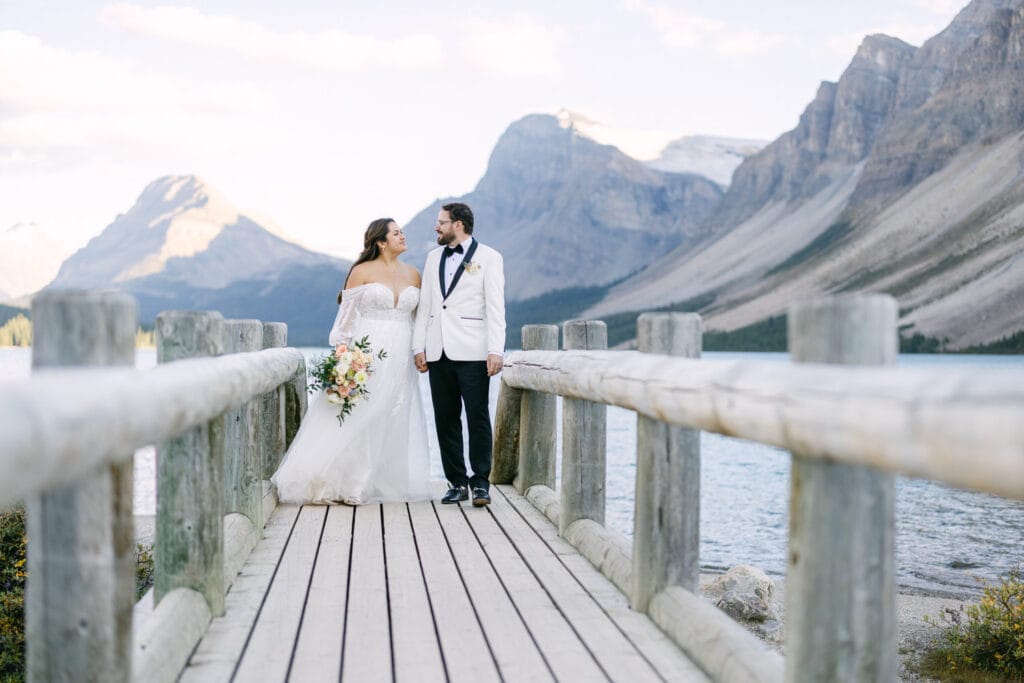 Bride and groom holding hands on a wooden jetty by a mountain lake