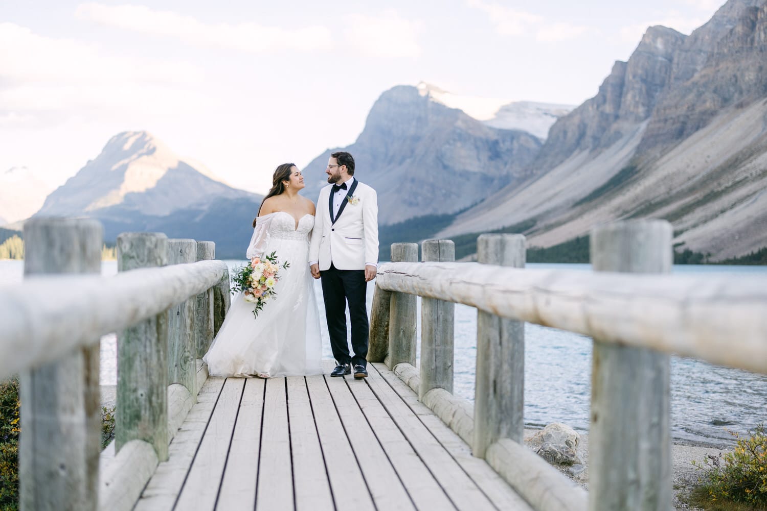 Bride and groom holding hands on a wooden jetty by a mountain lake