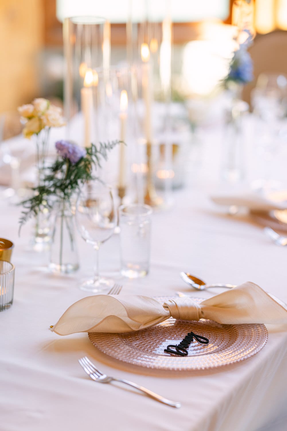 Close-up of a decorated dining table with candles, crystal glassware, and a neatly folded napkin on a charger plate.