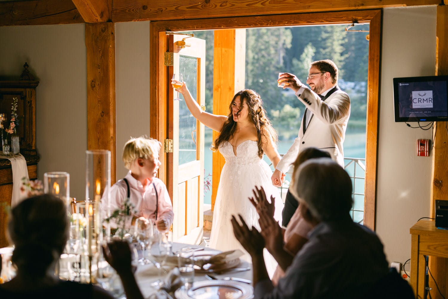 A bride and groom raising their glasses for a toast, surrounded by applauding guests at a wedding reception.