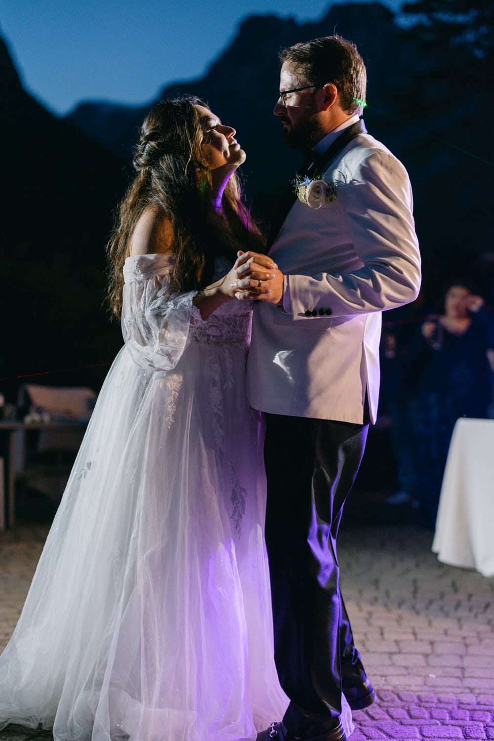 Bride and groom sharing a romantic dance outdoors at night with mountains in the background.