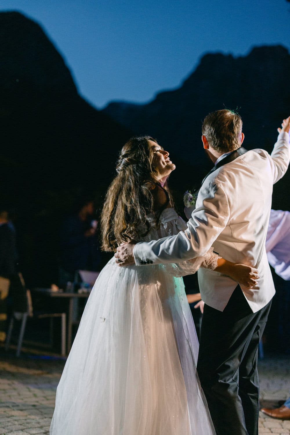 A bride and groom share a dance outdoors at night, with mountains silhouetted in the background.