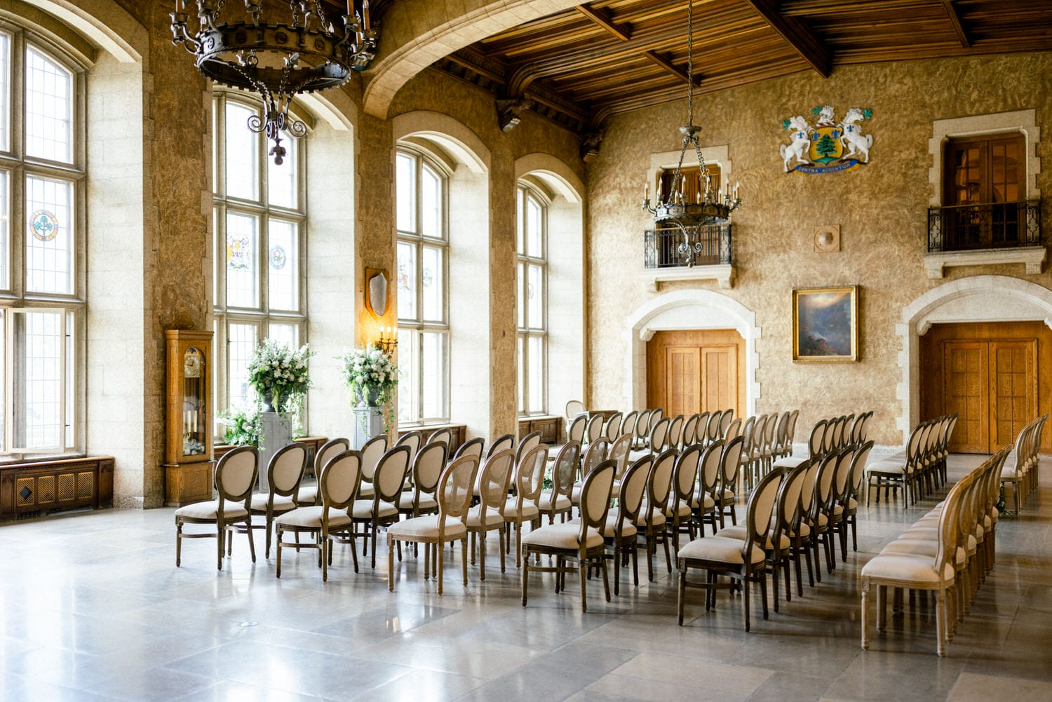 Interior view of a grand hall with arranged chairs, large windows, and ornate decorations ready for a formal gathering.