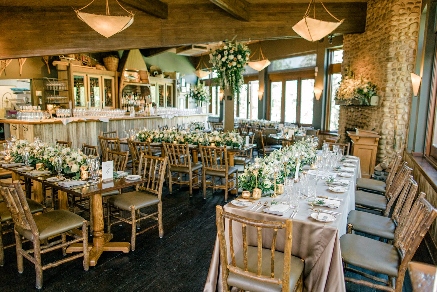 Interior view of a rustic-styled wedding reception with floral arrangements, set tables, and a bar area.