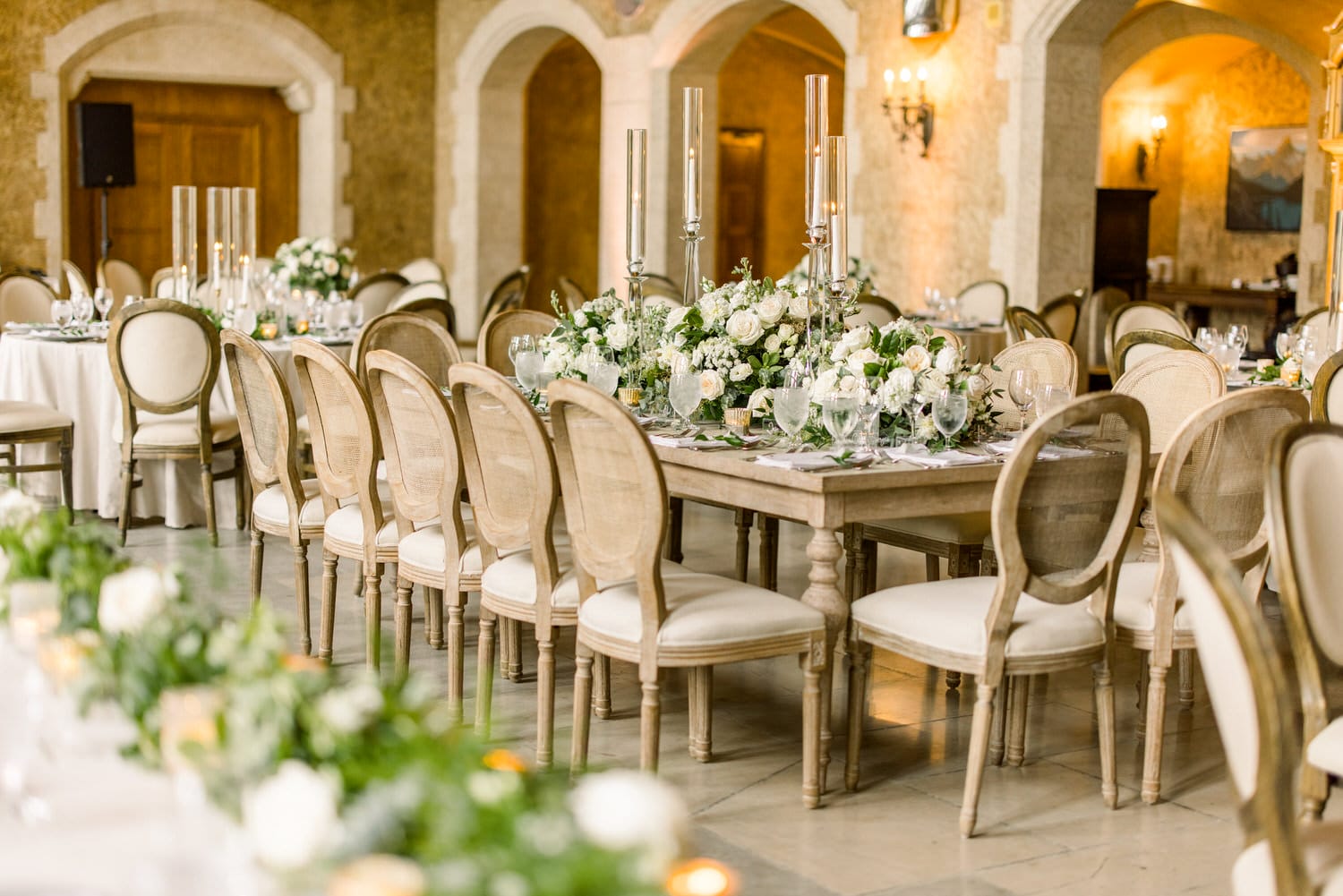 A beautifully arranged wedding reception table with floral centerpieces, candles, and elegant chairs in a luxurious venue.