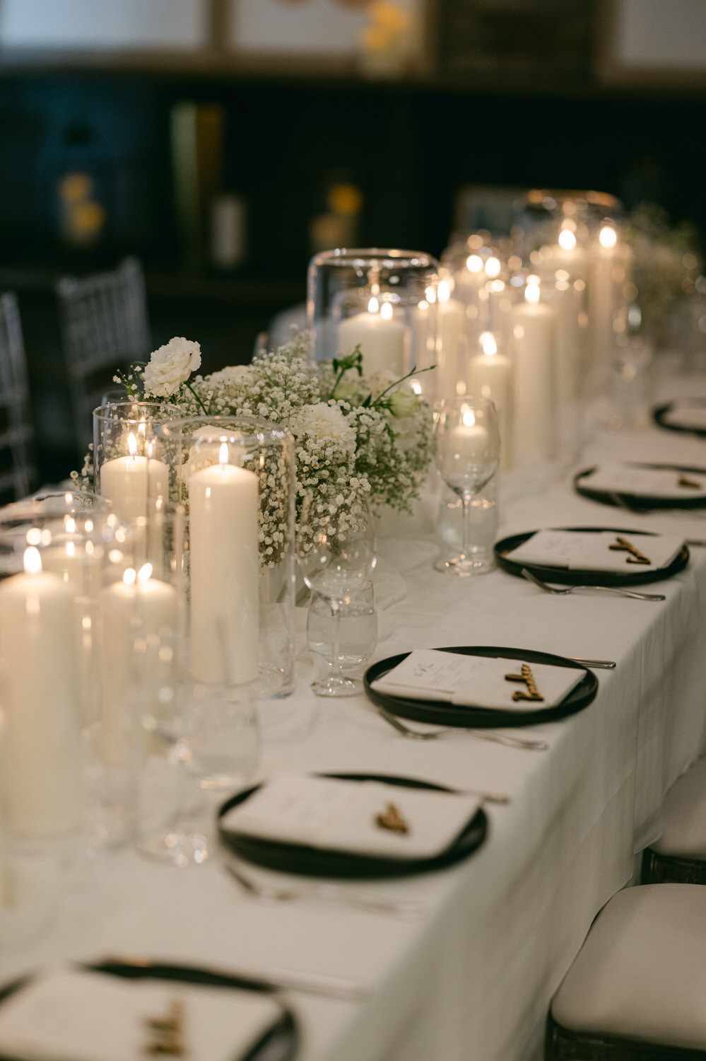 A beautifully arranged dining table featuring candles, delicate flowers, and black plates set for an intimate gathering.