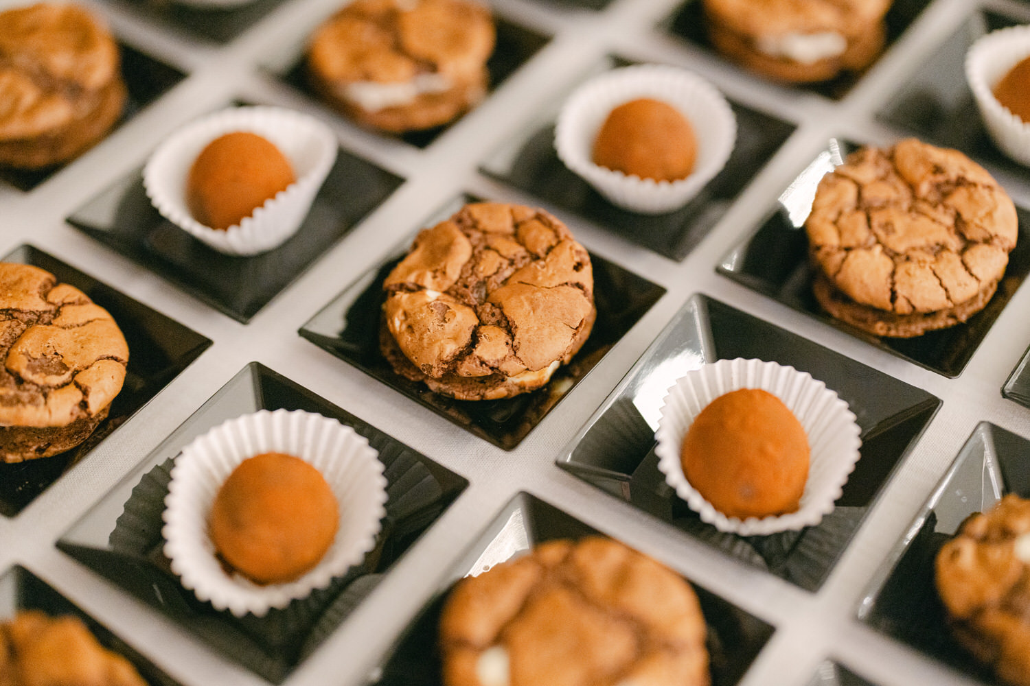 A close-up view of an elegant arrangement of chocolate cookies and round treats on black plates, showcasing a variety of desserts perfect for any occasion.