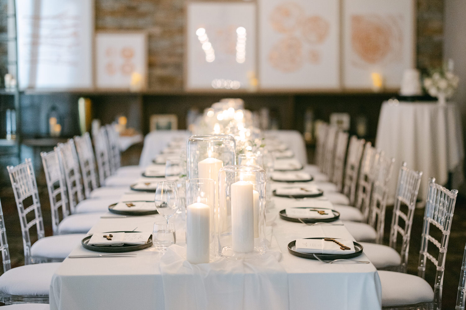 A long, elegantly set dining table adorned with white candles and decorative plates in a softly lit room.