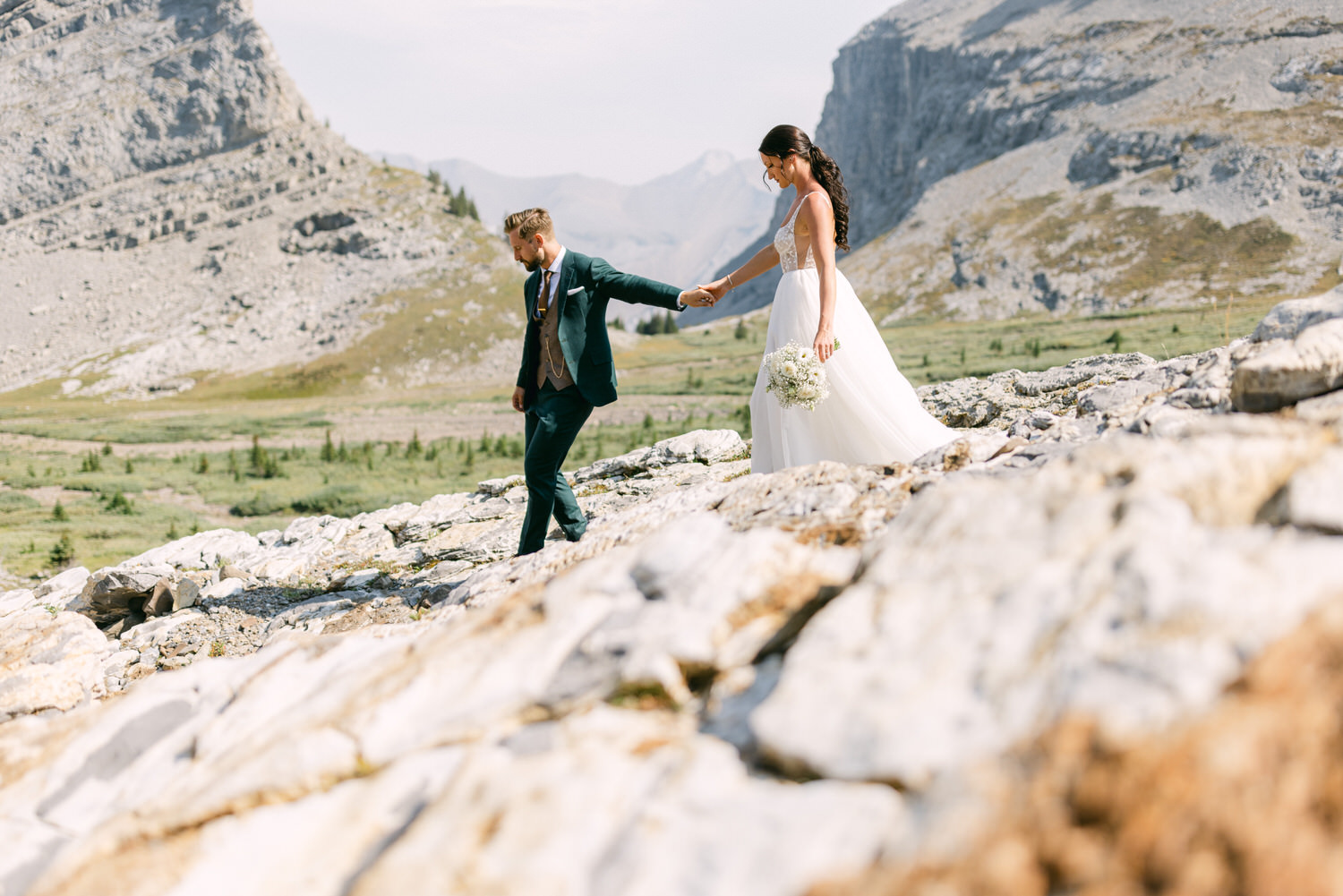 A couple holding hands while walking on rocky terrain, surrounded by breathtaking mountain scenery, capturing a moment of love and adventure.