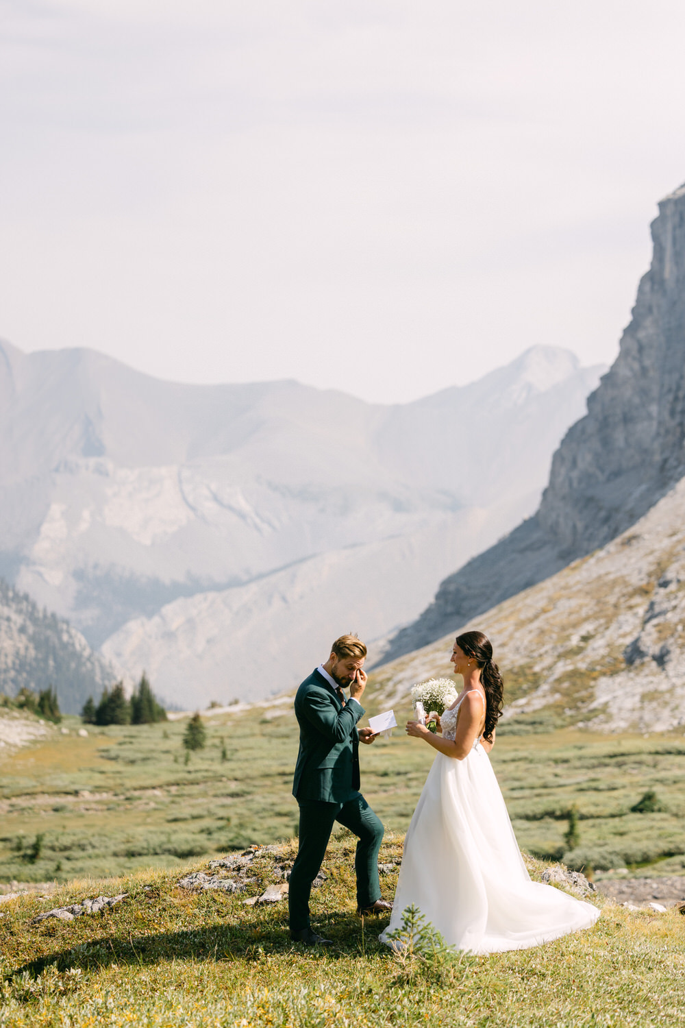 A couple exchanges vows in a picturesque mountain setting, surrounded by lush greenery and towering peaks.