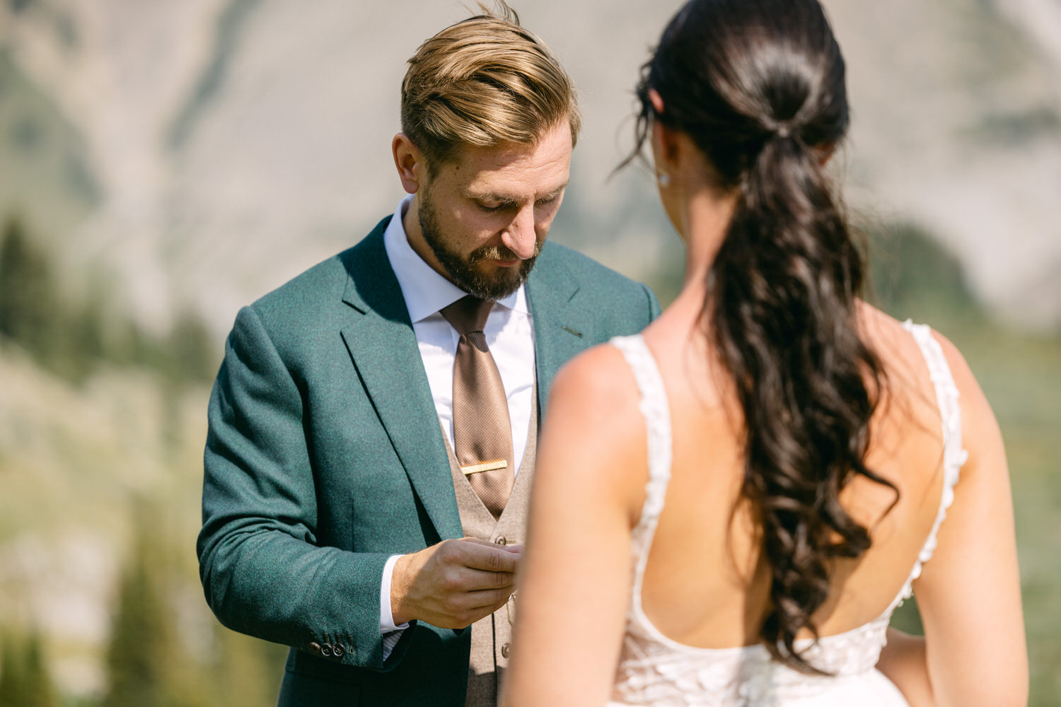 Groom placing a ring on the bride's finger during an outdoor wedding ceremony in a scenic setting.